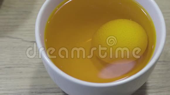 食物蛋用黄色染料着色放在桌子上的白色杯子里复活节装饰提示视频的预览图