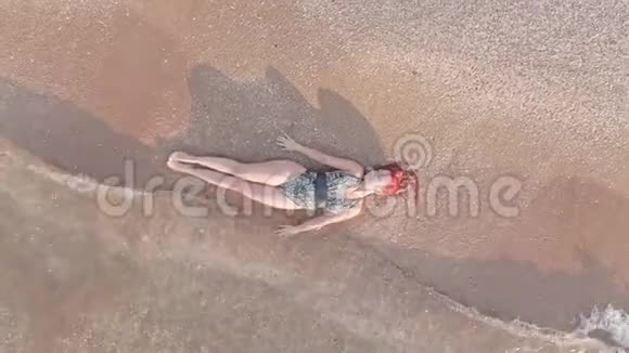 俯视图年轻女子穿着泳衣躺在沙滩上身体在抚摸海浪视频的预览图