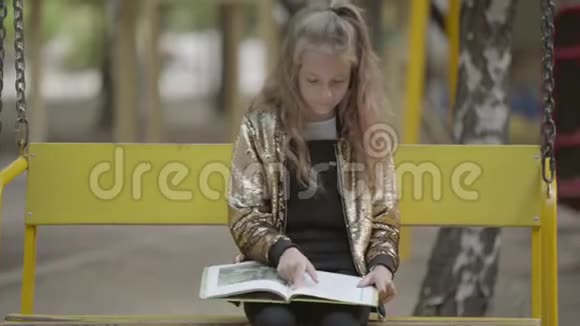 可爱的少女正在看一本书而坐在户外秋千上女孩用手掌捂住嘴视频的预览图