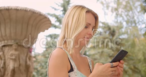 一位白种人成年女性正在等待她的男朋友并与他在公园里愉快地拥抱着用电话做了一幅特写照片视频的预览图
