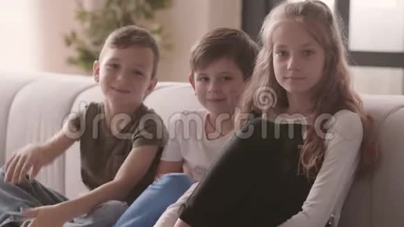 正面女孩和两个男孩坐在沙发上看着相机微笑的肖像兄弟姐妹关系视频的预览图