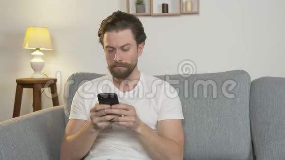一个年轻人独自坐在家里的沙发上与网上的人交流孤立地阅读新闻视频的预览图