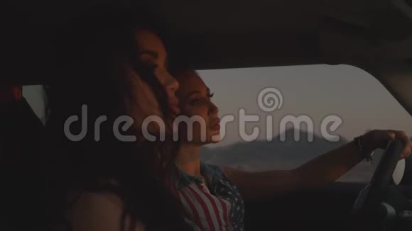 2坐在汽车里的两个年轻女人看日落从车窗里可以看到群山视频的预览图