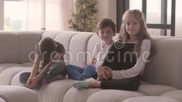 可爱的姐姐和两个弟弟坐在沙发上看着镜头微笑的画像视频的预览图