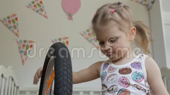 一个小女孩坐在孩子们房间里玩自行车转动轮子视频的预览图