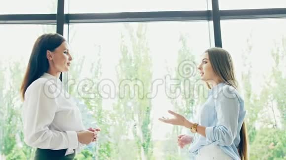 两个穿着商务服的女人正在办公室彩色玻璃窗的背景上交谈视频的预览图