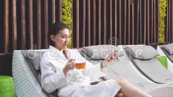 一位穿着白色长袍的年轻女性在一个现代的水疗中心里躺在躺椅上拍照视频的预览图