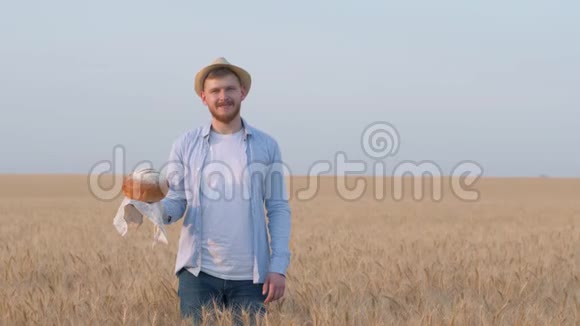 收获快乐的家伙手里拿着面包在秋天的季节用手展示着广阔的谷物麦田视频的预览图