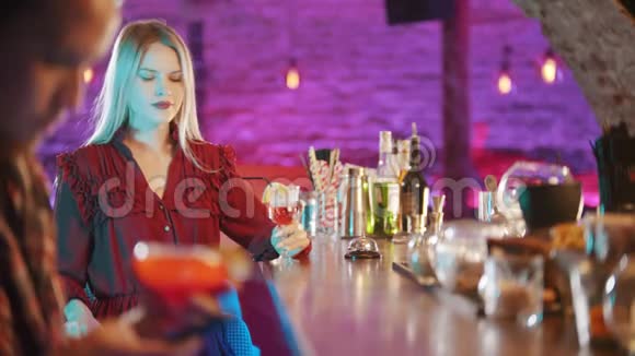 一位漂亮的金发女郎坐在酒保的旁边喝着吸管中的饮料一个男人坐在他的椅子上视频的预览图