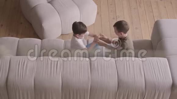 两个可爱的兄弟在沙发上互相嘲笑和打架小兄弟在家待着孩子们在愚弄视频的预览图