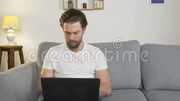 一个年轻人独自坐在家里的沙发上手提电脑上在网上找工作因为视频的预览图