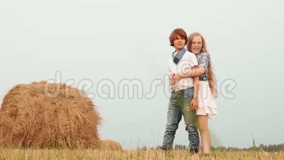 年轻夫妇在干草堆背景下拥抱在乡间田野上年轻夫妇的女孩和男孩拥抱视频的预览图