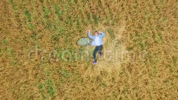 一个年轻的男人一个旅行者和一个搭便车的人躺在一个背包旁边在一小麦或黑麦播种的麦田里视频的预览图