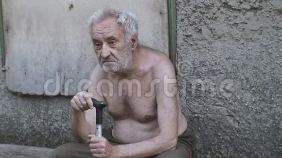 可怜的乞丐拿着拐杖坐在街上视频的预览图
