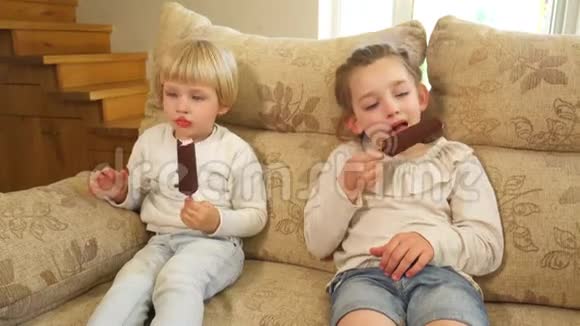 男孩和女孩在沙发上坐在木棍上吃冰淇淋和巧克力手持射击视频的预览图