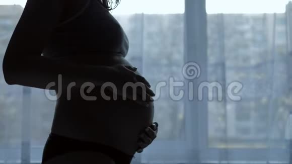 孕妇的剪影抚摸着她的胃抚摸着窗户视频的预览图