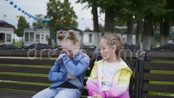 两个十几岁的女孩朋友在长凳上看着夹克口袋其中一个视频的预览图