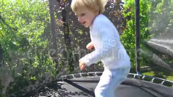 金发男孩在后院蹦床上跳慢动作视频的预览图