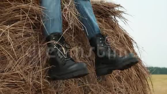 穿着牛仔裤和格子衬衫的少年男孩坐在乡间田野的干草堆上农村的肖像帅哥视频的预览图