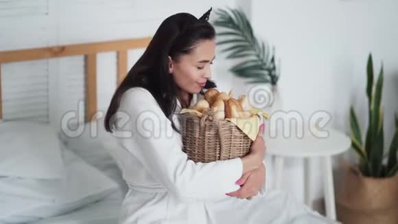 穿着白色浴袍的年轻女子手里拿着一篮子面包微笑着视频的预览图