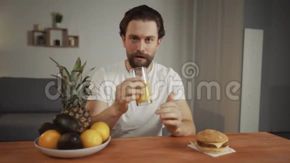 留着胡子的年轻人一边喝橙汁一边微笑一边选择健康的生活方式视频的预览图