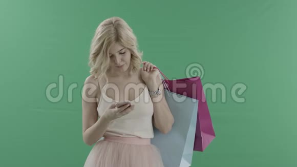 可爱的年轻女子在她的智能手机上发短信在绿色屏幕上拿着袋子等人视频的预览图