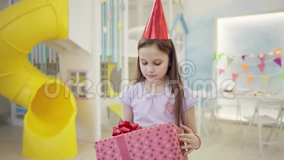 戴锥形帽子的不高兴的女孩在镜头前检查她的生日礼物视频的预览图