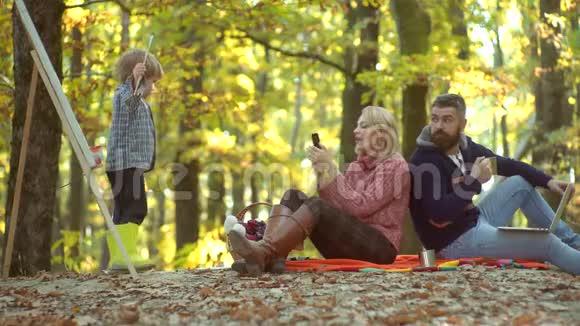 快乐的儿童艺术家在秋天的大自然中画画快乐的年轻夫妇和男孩在户外年轻父母和视频的预览图