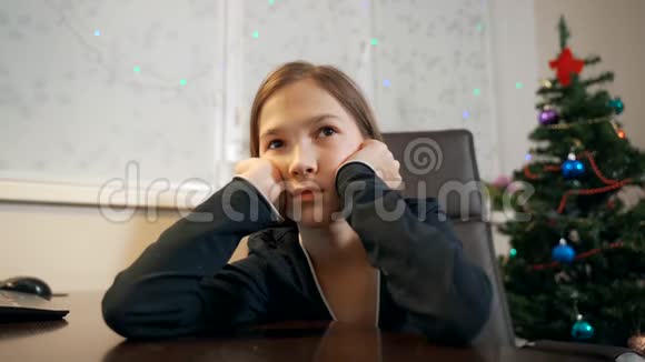 悲伤的女孩坐在圣诞树附近的一张桌子上双手抱着他的头视频的预览图
