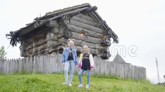 两个女孩少年站在绿色草坪上旋转童话屋少女在老巫婆的木屋上摆姿势视频的预览图