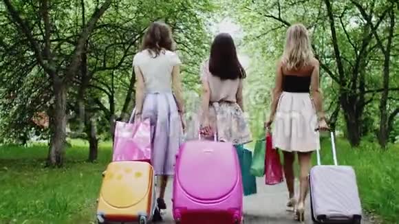 三个女孩带着手提箱度假公园里的购物袋后景视频的预览图