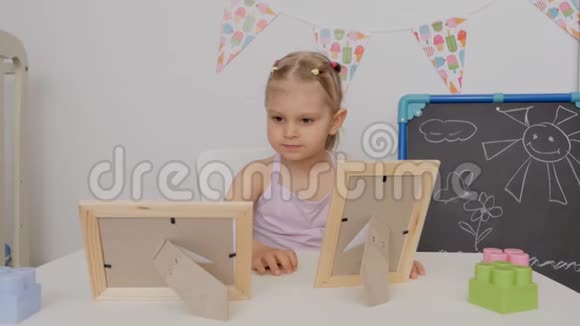 小可爱坐在孩子们的桌子旁看着相框里的照片视频的预览图
