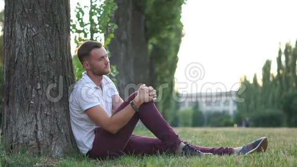 一个悲伤的家伙坐在树下慢动作的公园里视频的预览图