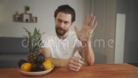 一个年轻人坐在桌子旁谈论水果的用处他拿起水果展示菠萝鳄梨视频的预览图