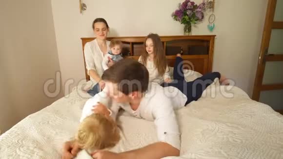 淘气的家庭妈妈带着孩子爬上爸爸躺在床上手持射击视频的预览图
