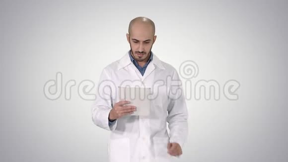 成熟男性医生拿着数字平板电脑使用它并在梯度背景下行走视频的预览图