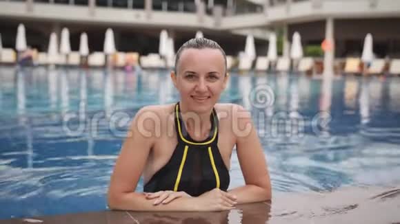 一个女人在游泳池边缘3040年的肖像那女人斜靠在池边微笑着看着视频的预览图