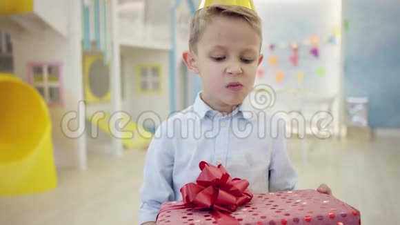 一个戴着生日锥帽满脸愤怒地看着自己礼物的沮丧的小男孩在镜头前视频的预览图