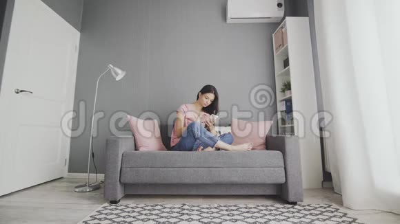 年轻可爱的女人在家里坐在沙发上用电话视频的预览图