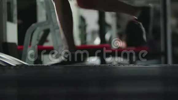 一个身材苗条的女孩在健身房黑暗的房间里的跑步机上从事体育锻炼的腿视频的预览图