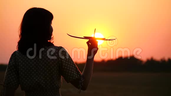 那个女孩梦想着旅行拿着一架模型飞机日落时幸福女人的剪影视频的预览图