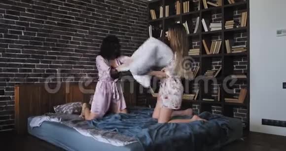 美丽的两个女人早上抱着枕头在床上打架她们感到兴奋和疯狂视频的预览图