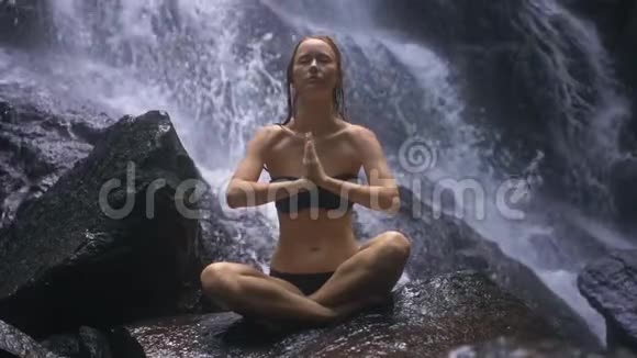 年轻女子坐在岩石上身后溅起瀑布视频的预览图