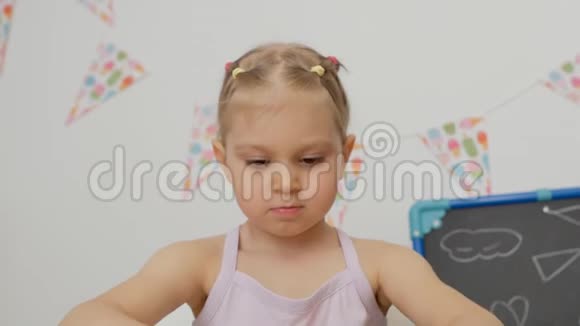 小可爱的女孩坐在孩子们的桌子旁房间里看着他的手沾满了明亮的油漆视频的预览图