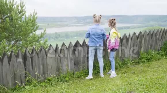 两个十几岁的女孩站在木栅栏边望着远处女孩们欣赏夏天的森林和河流视频的预览图