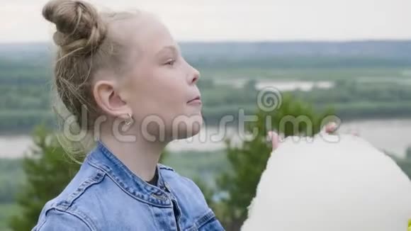 肖像少年女孩在夏天公园散步时吃甜棉花皮肤上有雀斑的红发女孩视频的预览图