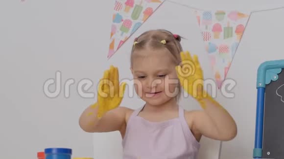 一个活泼开朗的小女孩坐在孩子们的桌子旁她的房间里用手指在纸上画画弄脏了她的手视频的预览图