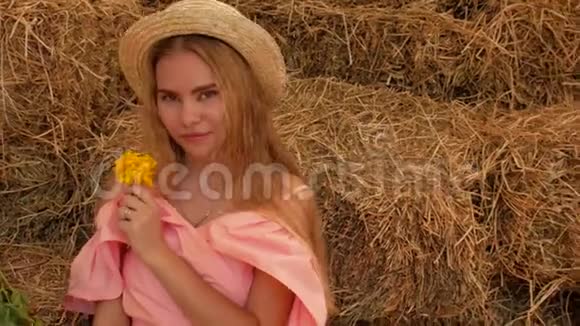 年轻迷人的女孩戴着草帽在干草和野花背景上对着镜头摆姿势微笑4k4k视频视频的预览图