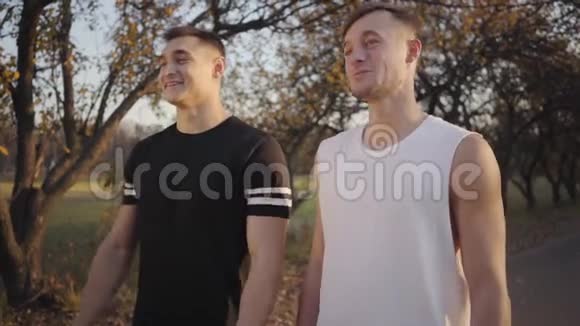两个穿着运动服的英俊的白人男孩站在秋天公园的阳光下交谈性奋的男人休息视频的预览图