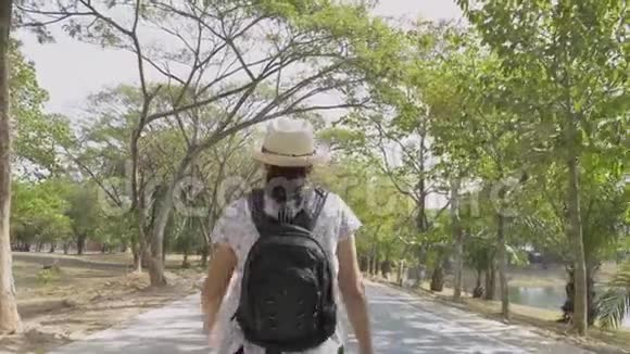 带背包戴草帽的亚洲女人的后景在公共公园的马路上行走视频的预览图